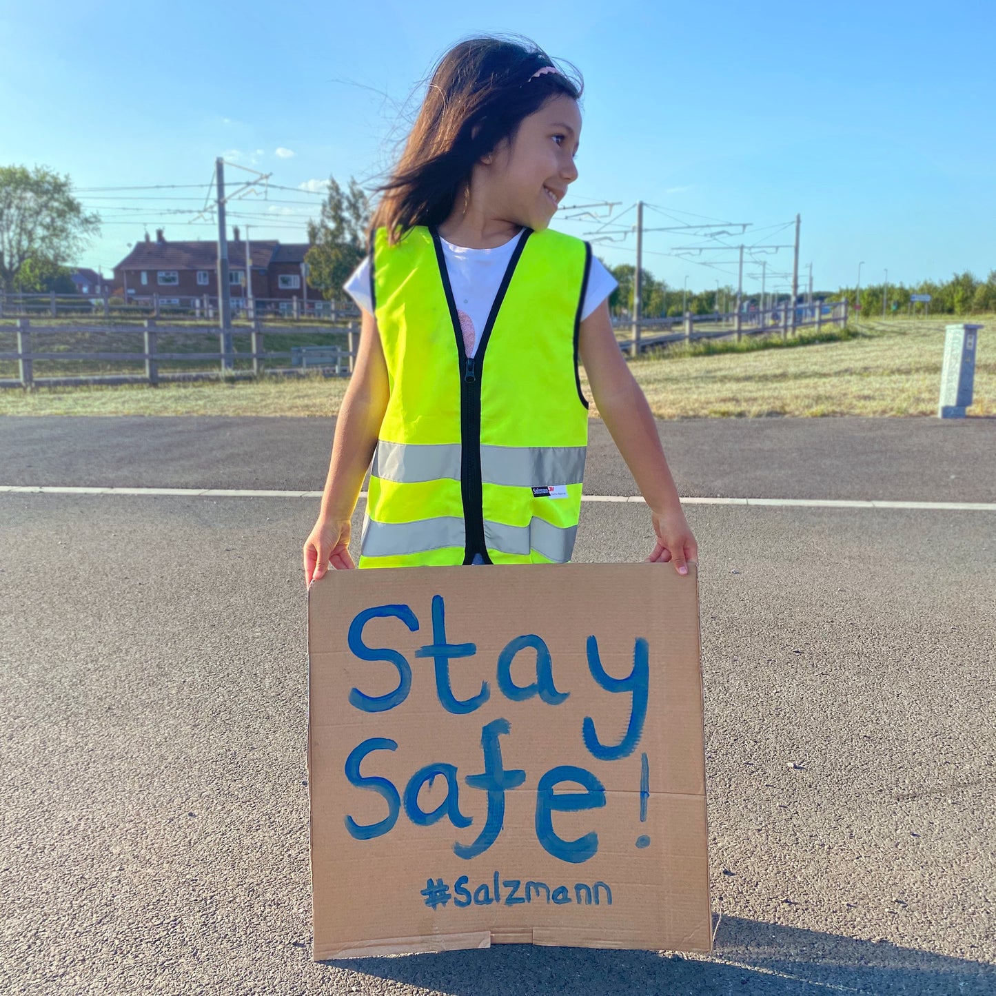 Kind trägt gelbe Salzmann Kinderwarnweste und hält Schild mit der Aufschrift "Stay Safe!"